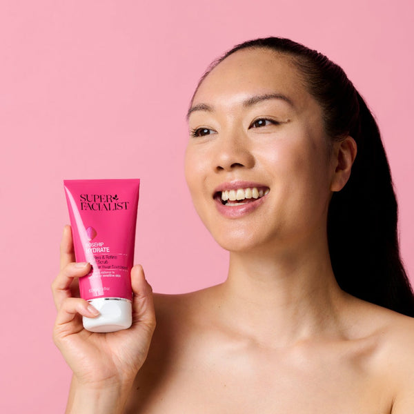 Smiling model holding the rosehip facial scrub in front of a pink backdrop