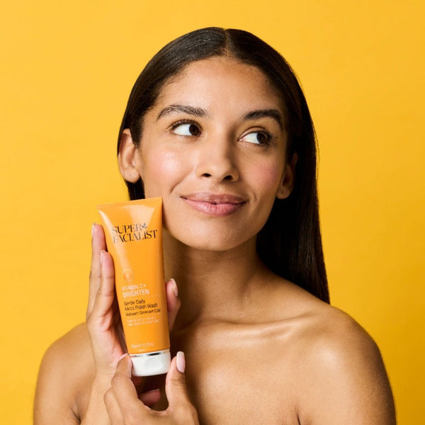 Model headshot holding vitamin c daily micro polish wash bottle while looking away